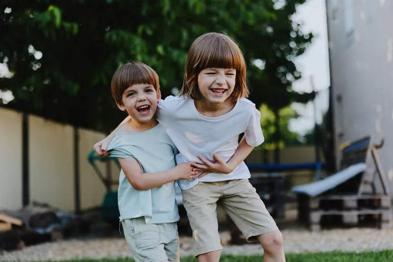 Two joyful children playing outdoors, showcasing a bond of friendship and happiness. They are wearing casual summer clothing, delighting in their playful moment.
