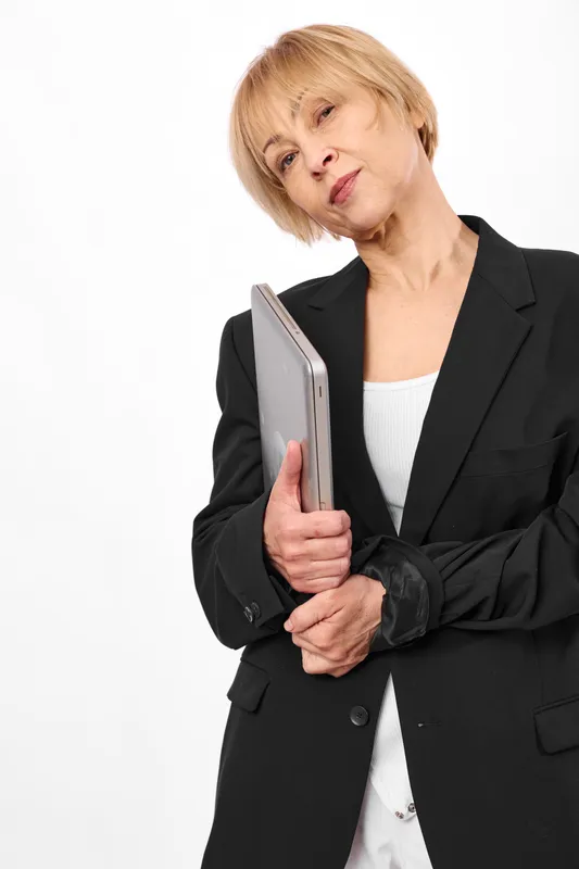 Elderly woman holding smartphone in formal blazer portrait on white background. She looks concerned while using mobile communication. Concept of technology for seniors, indoors.