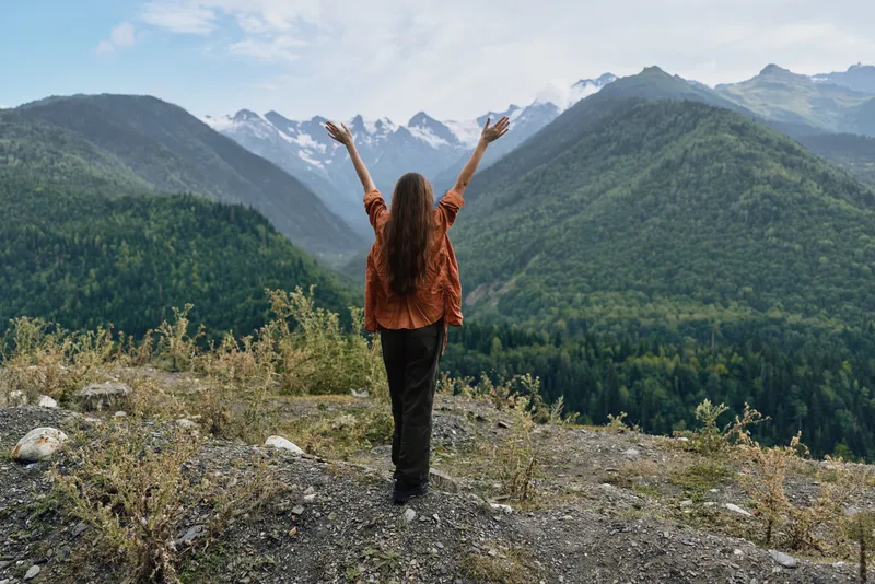 Woman on mountain ridge, nature landscape hiking outdoors, arms raised for freedom authenticity inclusivity, joy