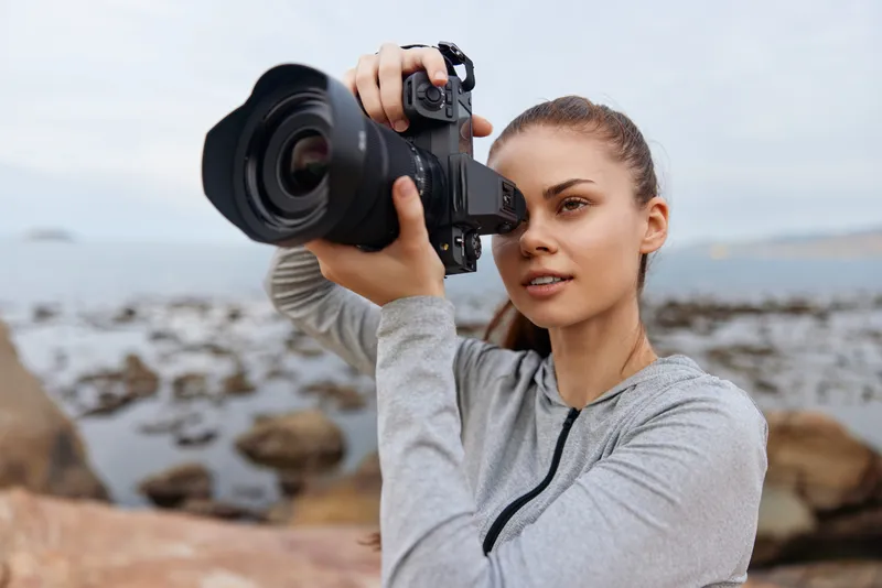Young woman photographing scenic landscape with DSLR camera by the sea, showcasing passion for photography and adventure in a natural setting