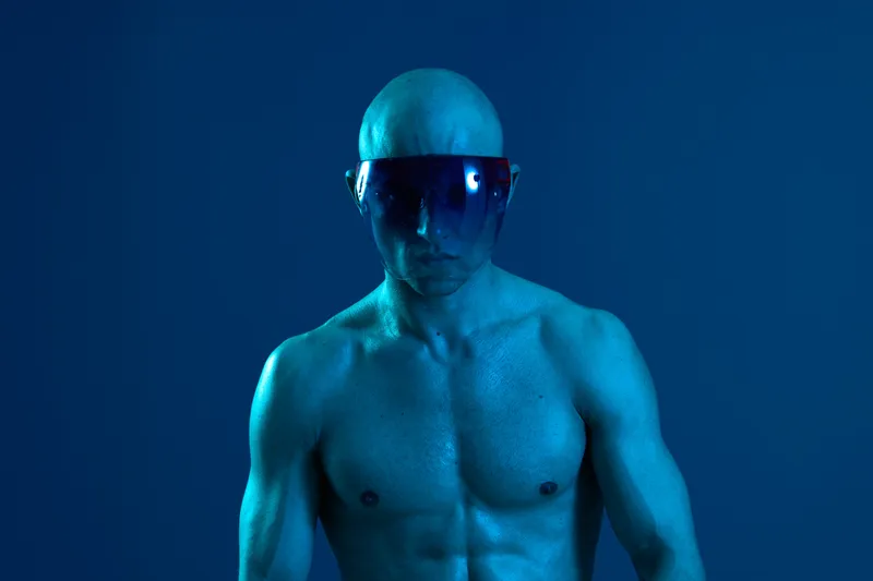 Strong man with futuristic visor, blue lighting enhances intense expression and striking physique. Perfect for themes of technology and strength in creative visuals.