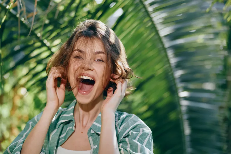 Woman outdoors with a bright smile, joyful energy shines through the candid portrait, natural light highlights her cheerful mood amid lush greenery around, vibrant and lively.