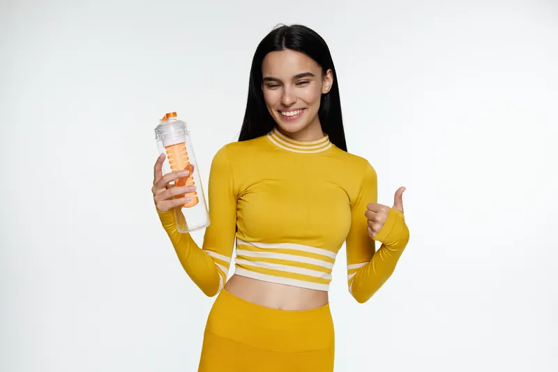 Sport fitness woman in yellow activewear holding a water bottle, smiling, showing thumbs up, healthy lifestyle, hydration, positive energy.