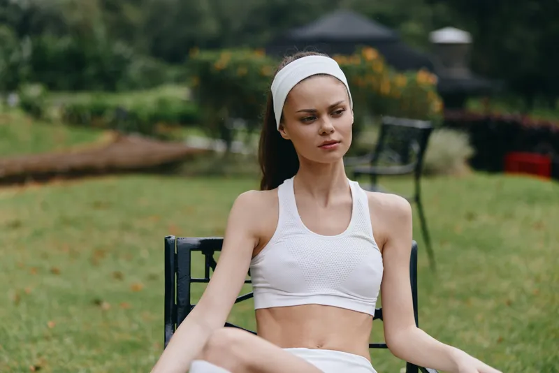 Young woman in sportswear practicing mindfulness outdoors, radiating serenity in a lush green garden, promoting wellness and tranquility during a sunny day