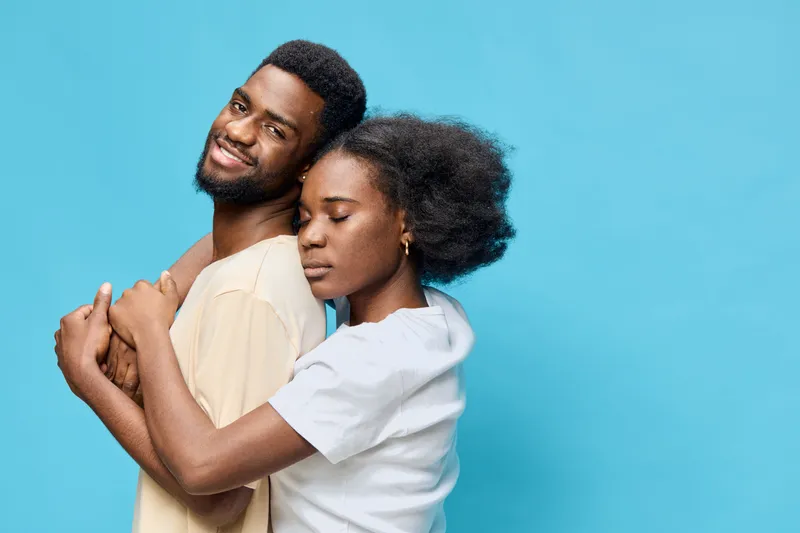 Young African couple embracing each other, showcasing love and connection against a bright blue background, ideal for themes of romance, relationships, or emotional bonds
