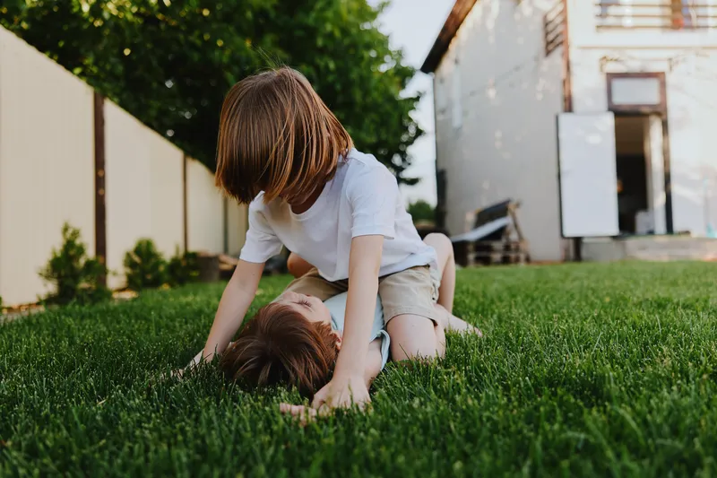 A cheerful boy having fun with a girl in a sunny backyard, playing on the green grass. Their laughter fills the air as they enjoy their playful moment together.