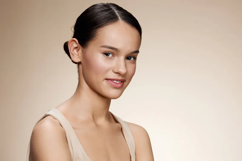 Portrait of a young model with a natural, serene expression, showcasing healthy skin and minimalist makeup against a soft beige background
