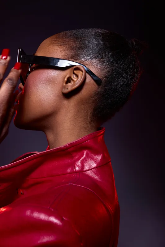 Profile of a stylish African woman with dark skin wearing black glasses and a red leather jacket. Concept of fashion, beauty, and modern urban style with confident attitude.