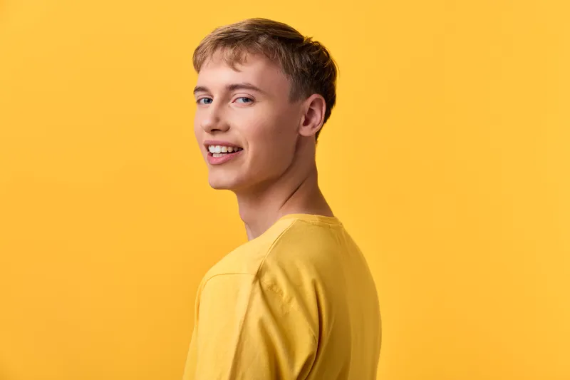 Smiling male model in a yellow shirt poses against a bright yellow studio backdrop, radiating warmth, positivity, and casual confidence for lifestyle or fashion use
