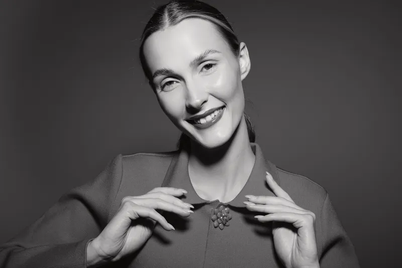 Smiling Caucasian woman with fair skin and pulled back hair in vintage style dress posing in black and white studio portrait.