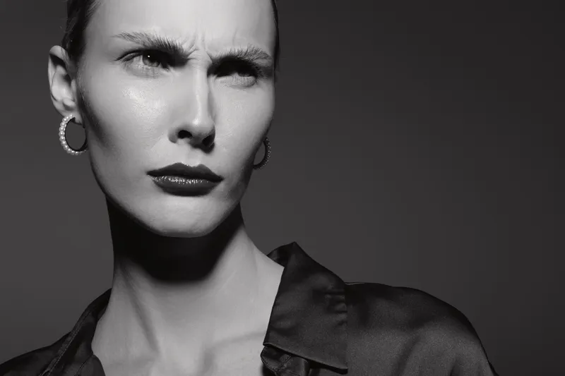 Close-up portrait of a serious caucasian woman with fair skin looking confused or skeptical. Black and white image with dramatic lighting and high contrast.