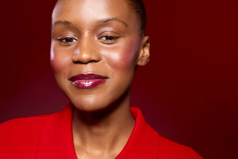 Close-up portrait of confident dark skinned African woman with shiny skin and glossy lips wearing red clothing against red background. Concept of beauty, fashion, and self-confidence.