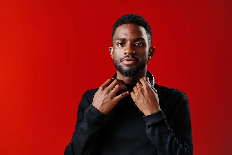Confident young Black man in a black hoodie, against a vibrant red background, showcasing modern fashion and self assurance with an engaging expression