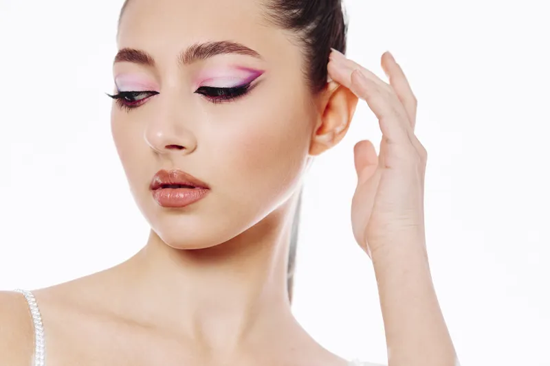 Close-up of woman with creative purple eyeliner fashion makeup looking down. Soft natural skin tones and smooth hairstyle on white background. Concept of beauty and style.
