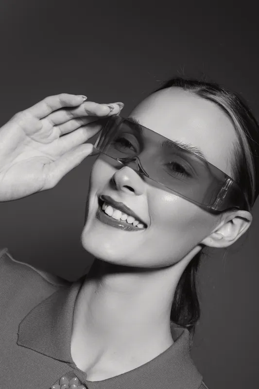 Young Caucasian woman with fair skin wearing stylish sunglasses smiles confidently against dark background. Concept of fashion, beauty, and modern eyewear accessories.