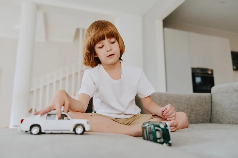 A focused boy playing with toy cars, showcasing creativity and imagination. Bright, playful atmosphere with modern interior elements.