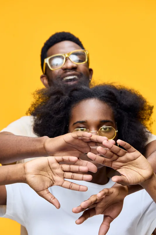 Two diverse models joyfully posing in front of a vibrant yellow background, showcasing unique styles and playful emotions, perfect for modern lifestyle concepts