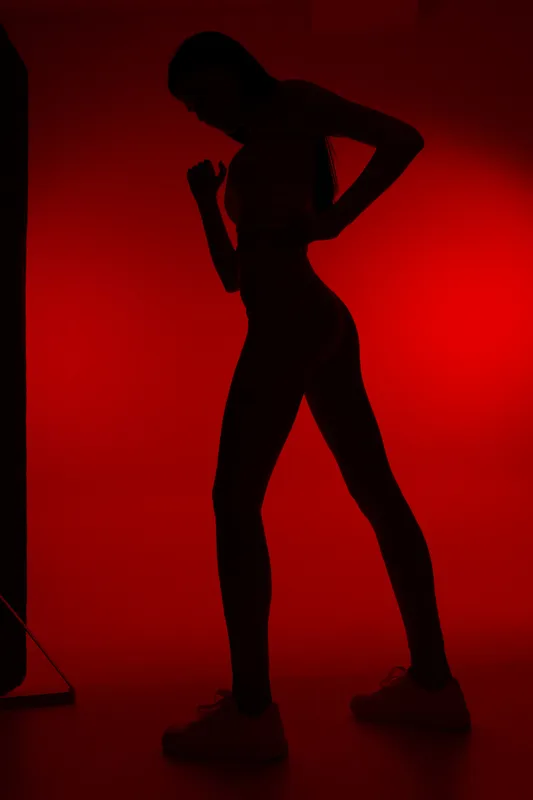 Silhouette of a woman sport fitness figure in activewear posing against a red background, showcasing strength, endurance, and athletic body shape.