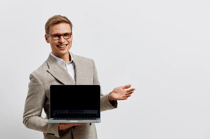 Smiling professional man in glasses and suit presenting laptop computer isolated on plain white background. Business concept, modern technology, success, confidence, communication, workspace.
