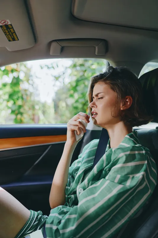A woman sits in a car, relaxed and thoughtful, wearing a green striped shirt as sunlight pours through the window.