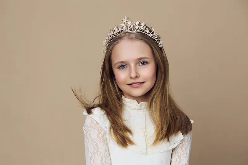 Young girl with a crown in a light dress against a neutral background, exuding joy and innocence, perfect for children s portraiture and princess themed projects