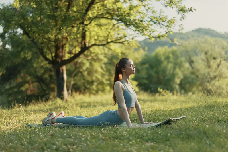 Young woman practicing yoga outdoors in a serene natural setting, wearing a light blue athletic outfit, embodying peace and mindfulness