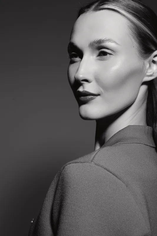 Portrait of a young Caucasian woman with light skin and slicked back hair, looking sideways with soft studio lighting.