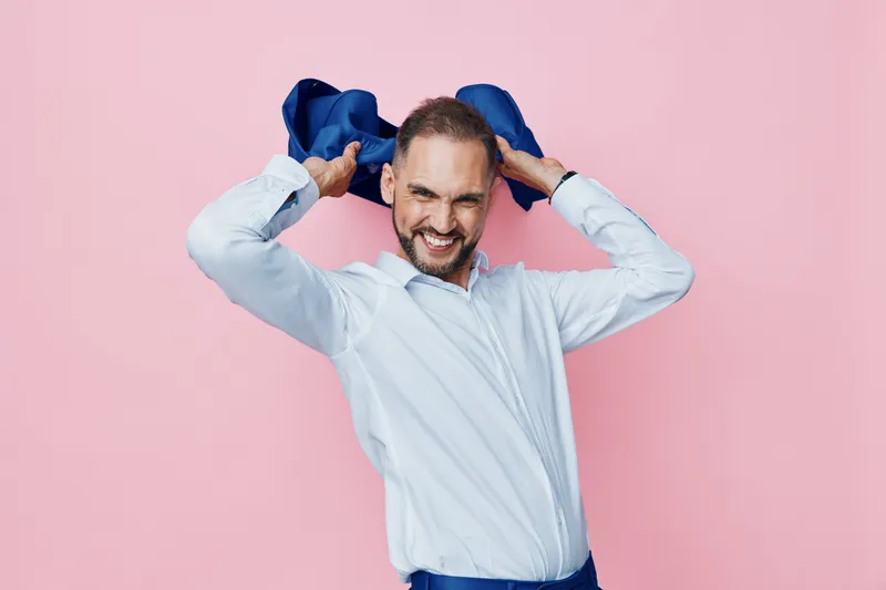 A confident business man stands against an isolated colorful background, exuding professionalism and strong emotion as he adjusts a blue accessory with a friendly, energetic smile.