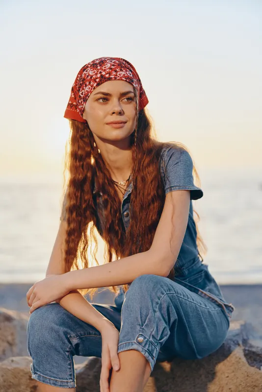 Lifestyle woman in modern boho-western denim street style with a red bandana, casual layered jewelry, and natural sunlight capturing a relaxed film color mood.
