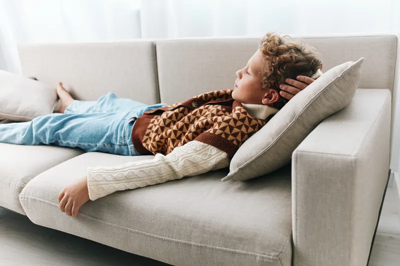 Authentic student lifestyle moment shows a relaxed learner on a couch in casual school attire, highlighting authenticity and a gentle theme of play and study.