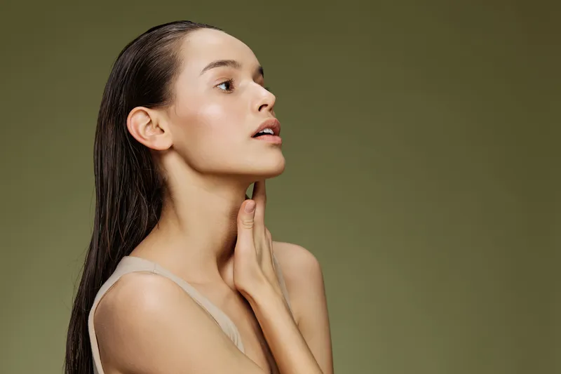 Elegant model with long hair, wearing a minimalistic outfit, showcasing a serene expression against a soft green background emphasizing natural beauty and simplicity