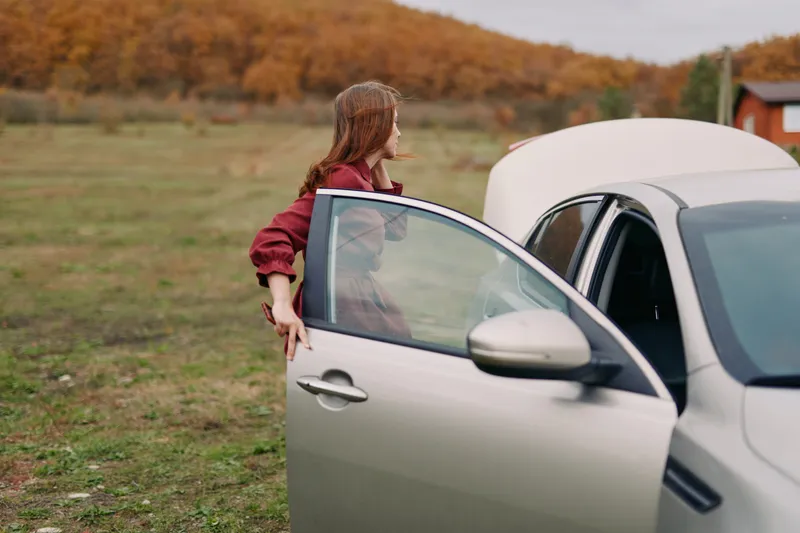 A candid scene of a woman inspecting her car with the hood open on a rural roadside, conveying authentic problem-solving and trustworthy self-reliance in a natural setting, ?????????????.