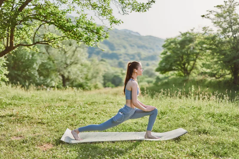 Young woman practicing yoga in a serene natural setting, wearing light blue activewear, showcasing a peaceful emotion during a summer morning workout
