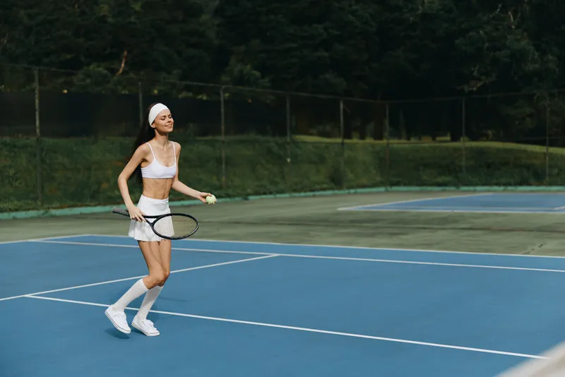 Young athletic woman playing tennis on a blue court, dressed in a sporty outfit, exuding joy and energy while enjoying her game in a vibrant outdoor setting
