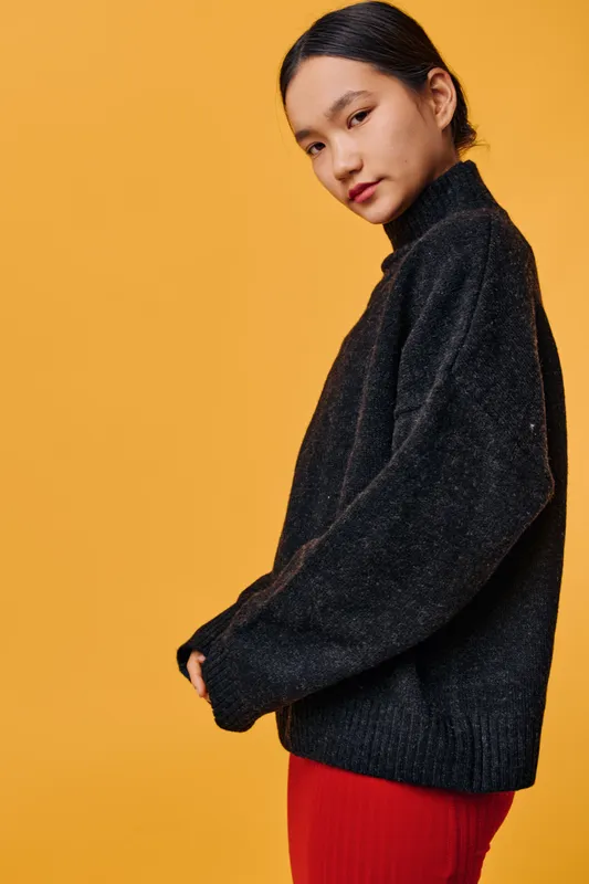 Young woman in black sweater posing with side glance on orange background. Fashion portrait with casual outfit and natural look for style and beauty concept in studio.