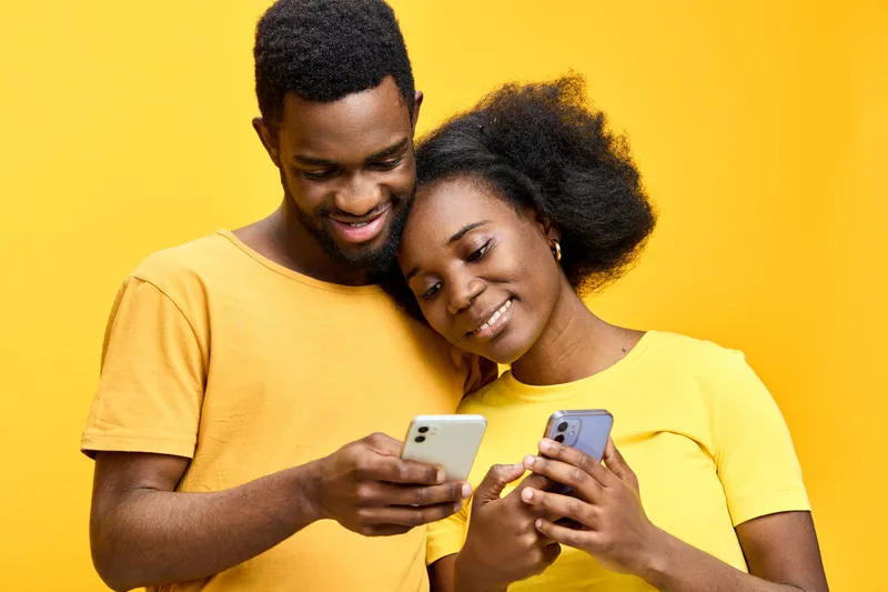 Happy couple using smartphones together, sharing moments with bright yellow background, showcasing connection, joy, and modern technology