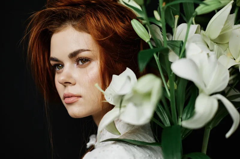 A serene young woman with red hair, surrounded by white lilies, exudes a natural elegance and calm, perfect for themes of beauty and emotional connection