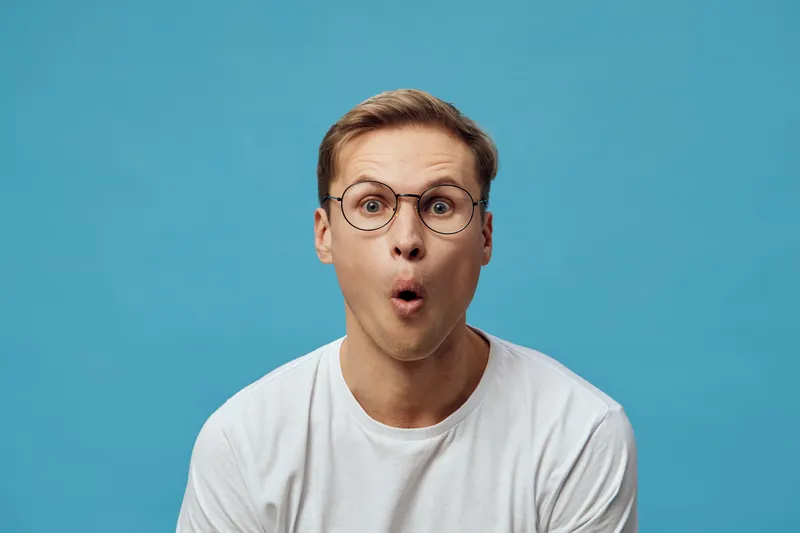 surprised young man wearing glasses white t-shirt looking amazed astonished isolated on blue background digital detox concept