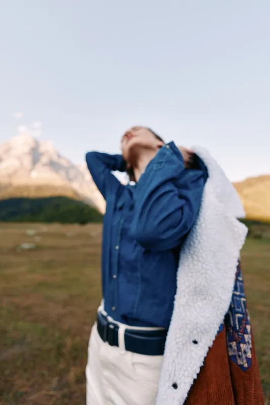 woman mountain nature jacket denim travel outdoors portrait of young model in field, casual style with coat over shoulder, looking up to sky in scenic landscape for adventure and relaxation