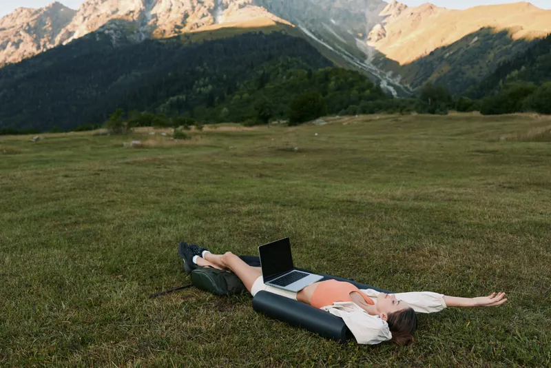 A relaxed professional lies on a grassy field with a laptop, enjoying outdoor work moments. The scene conveys calm focus, creative freedom, and productive energy in nature.