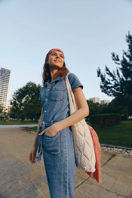 lifestyle woman in modern boho-western denim street style with a knitted tote bag, smiling outdoors in film color tone, casual fashion look urban setting