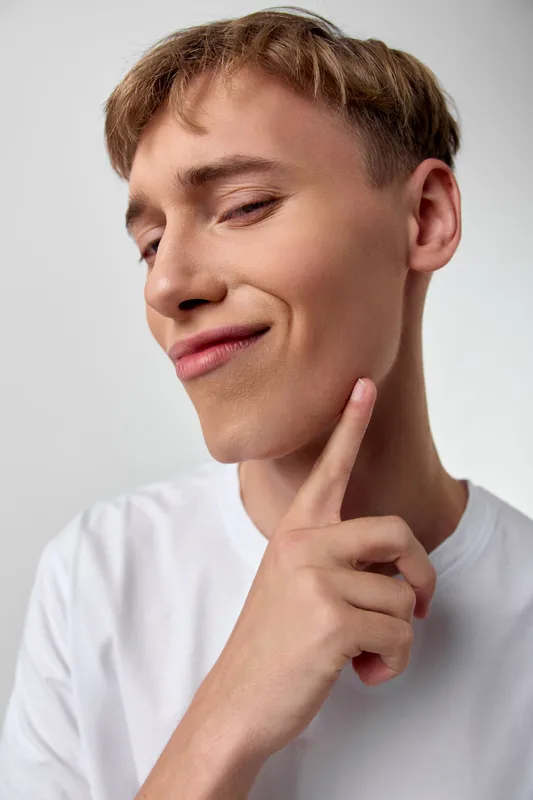 Thinking man in a casual white tee with a thoughtful pose, chin resting on finger, soft lighting and closeup framing for a calm, reflective mood