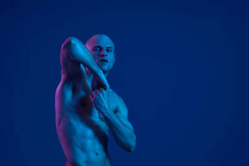 Fit man striking a pose against a blue backdrop, showcasing strength and confidence. This striking image uses vivid lighting to enhance the visual impact.