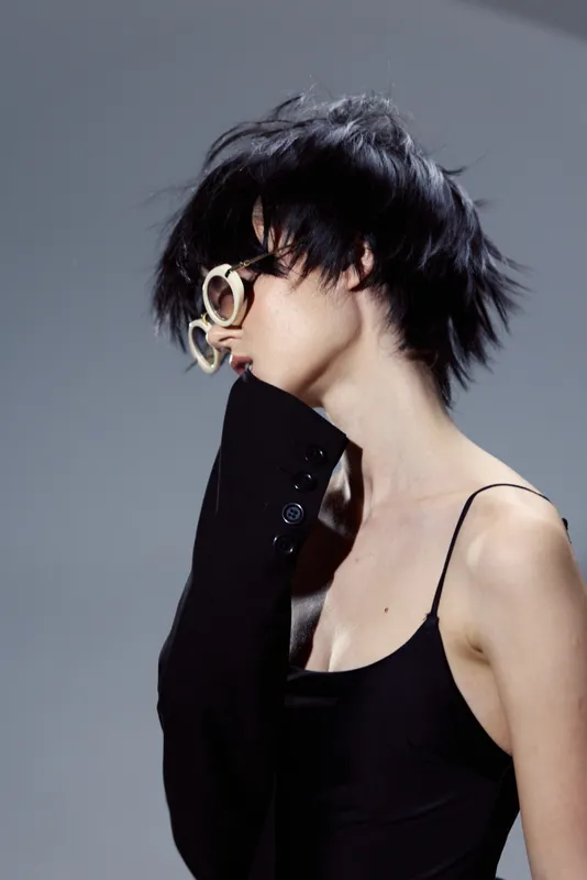 Stylish woman with short black hair wearing sunglasses and a black dress in minimalist lighting