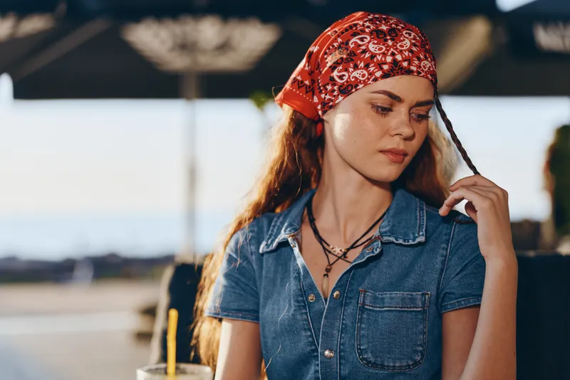 Lifestyle woman in modern boho-western denim street style wearing a red bandana and casual necklace, captured with warm film color tones in natural light.