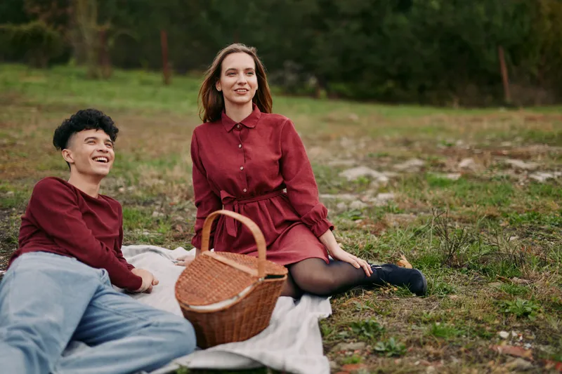 Natural, authentic portrait of a young couple enjoying a relaxed outdoor picnic on a blanket with a wicker basket, genuine expressions and candid body language with authenticity.
