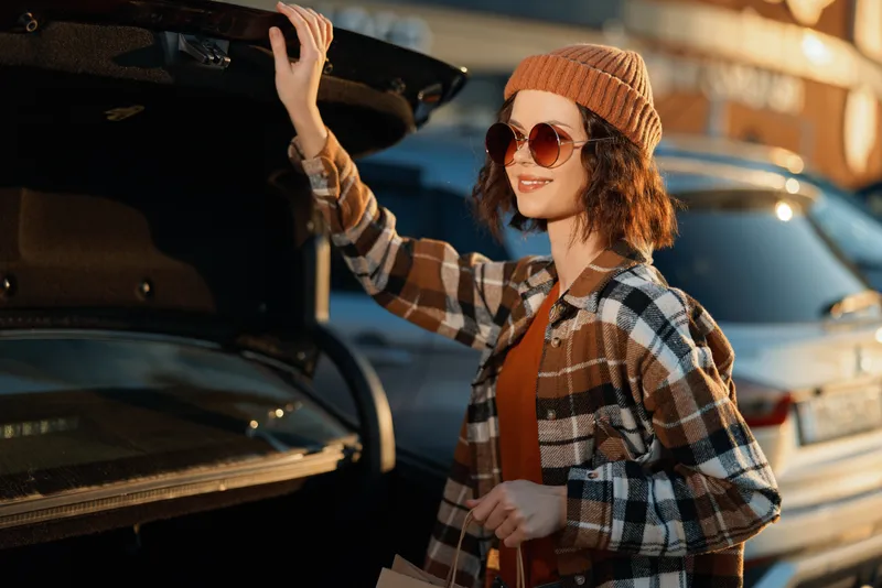 Woman car trunk shopping autumn portrait sunglasses beanie in golden hour glow, candid lifestyle authenticity and mindful living captured with emotional storytelling and urban warmth.