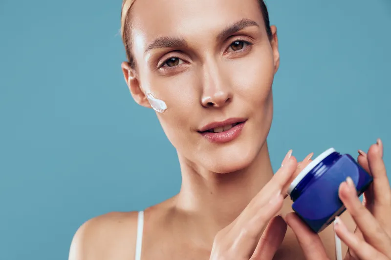 A confident young woman applies moisturizer to her cheek in a close up shot, showcasing a focused skincare routine and self care moment for healthy daily rituals.