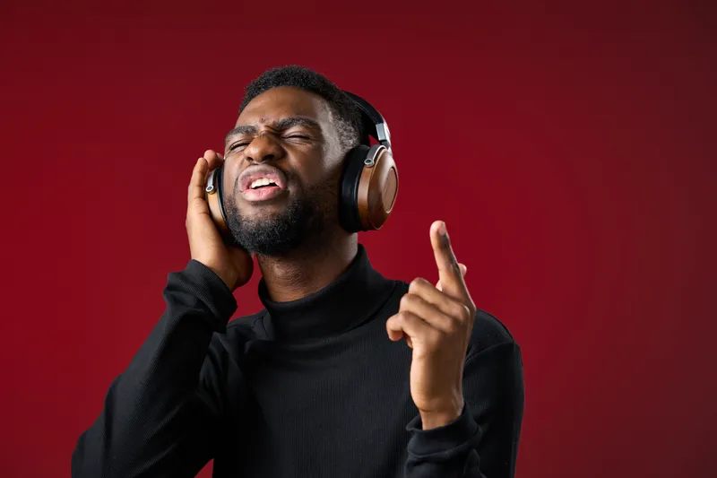 Young African man enjoying music with headphones, expressing joy and enthusiasm against a vibrant red background