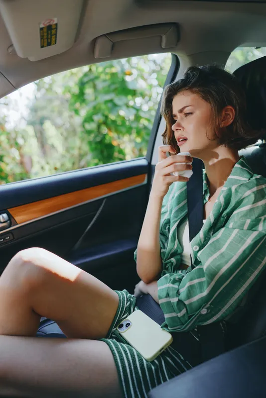 A woman sits in a car interior, relaxed and contemplative, wearing a green striped shirt, seat belt fastened, natural light highlighting her calm mood and readiness for a journey.
